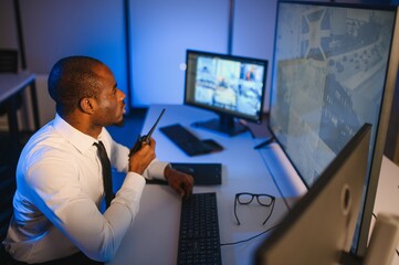 African American security officer or dispatch uses computer and walkie talkie, looks at screens