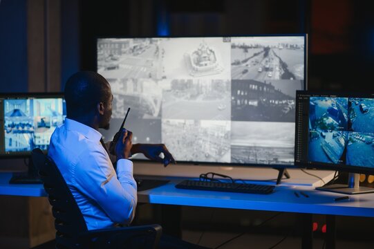 Back view of African American security operator use computer with screens showing surveillance camera footage