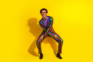 Young man in vibrant striped suit posing against yellow background expressing happiness, individuality
