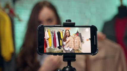 Young female blogger live streaming in her local fashion store, stylist and designer showing cashmere jacket for her online virtual audience, concept of online selling and small business