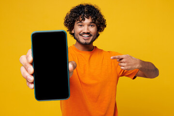 Young Indian man wear orange t-shirt casual clothes hold in hand use point on mobile cell phone...