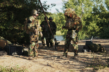 A group of troops in full military gear secures the army base, equipped with long rifles,...