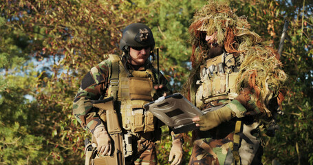 Fototapeta premium Soldiers dressed in full combat gear review the terrain map on an armored laptop, discussing strategy and finalizing mission details before heading into action.