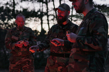 Fototapeta premium Four military men in full camouflage uniforms stand by a bonfire, talking, exchanging experiences, and unwinding after work and field exercises.