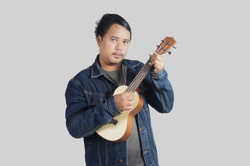 a southeast asian man is playing the ukulele very energetically with plain background     