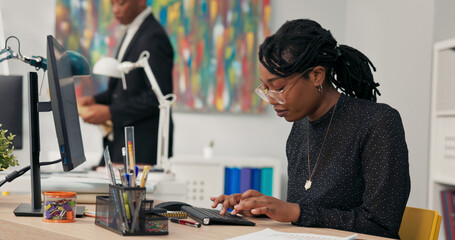 Beautiful woman with glasses dark-skinned company secretary sits in office in front of computer tapping fingers on keyboard writing e-mails filling out documents reports preparing minutes for manager