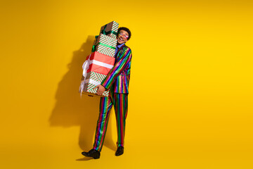 Charismatic young man in colorful suit holding gift boxes with vibrant yellow background, celebrating festive moments