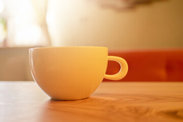 A ceramic cup rests on a smooth wooden table, illuminated by soft afternoon light. The warm ambiance suggests a perfect spot for enjoying beverages and relaxation