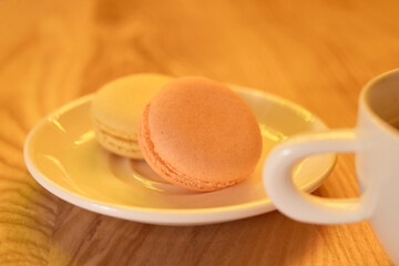 Two colorful macarons rest on a small plate next to a steaming cup of coffee, creating a warm and inviting ambiance in a cozy cafe. Perfect pairing for an afternoon treat
