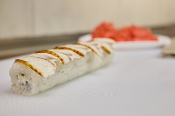 A sushi roll featuring grilled fish is presented on a white plate, accompanied by fresh watermelon slices. The restaurant has a clean, minimalist atmosphere, enhancing the food's appeal