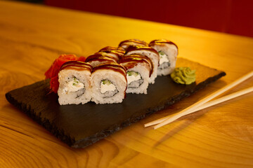 Fresh sushi rolls filled with cream and vegetables are stylishly presented on a black stone plate....