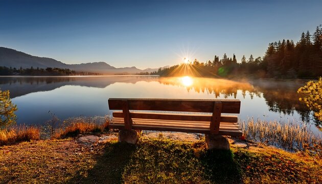 A wooden bench beside a peaceful lake at sunrise.