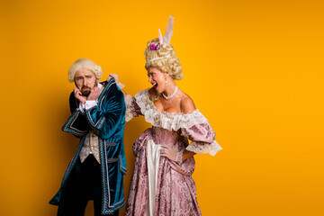 Elegant couple in vintage costumes celebrates in front of a yellow backdrop
