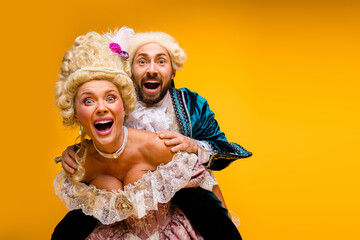 Amusing couple in vintage royal costumes against vibrant yellow background showcasing a blend of...