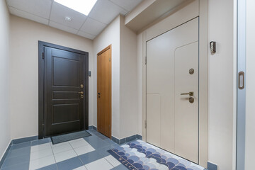 Hall with light beige walls, blue tile floor. Entrance iron doors with door mats.