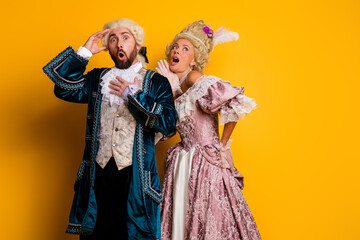 Fototapeta premium Elegant couple in historical costumes displaying expressions against yellow background