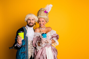 Fototapeta premium Couple in retro royal costumes enjoying modern coffee mugs against a vibrant yellow background