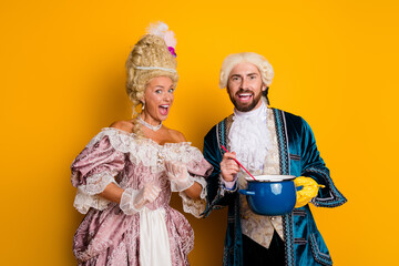 Couple in elaborate historic costumes posing in front of a yellow background with vibrant...