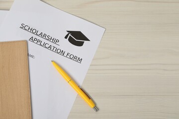 Scholarship application form and pen on wooden table, flat lay. Space for text