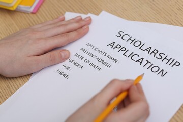 Student filling scholarship application form at wooden table, closeup