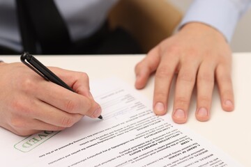 Man signing licensing agreement document at white table indoors, closeup