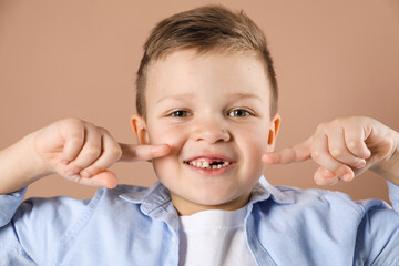 Cute little boy pointing at his missing tooth on dark beige background