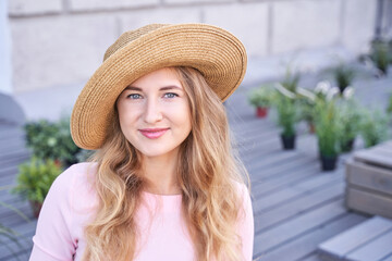 Young caucasian woman in straw hat smiling outdoors surrounded by plants.