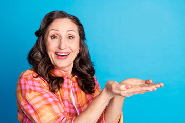 Happy mature woman with cheerful expression gesturing invitingly, isolated on blue background