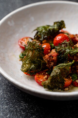 A beautifully arranged plate features fresh cherry tomatoes, crispy kale, and a blend of savory ingredients, creating a delightful dish that excites the senses during a fine dining experience