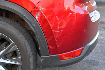 Close-up of scratched rear bumper on red car, visible paint damage, scuff marks, indicating need...
