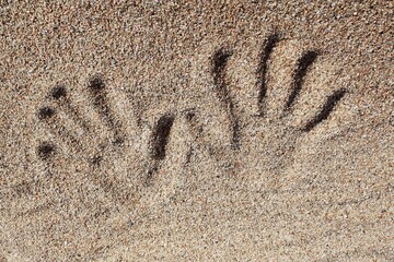 Handprint and fingerprints on sand surface. Imprint of hand in sandy texture. Human hand and finger marks in sand. Impression of a hand on sand. Sandy background with hand and finger traces
