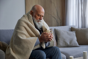 Sick weak senior man feeling unwell drinking tea sitting on sofa