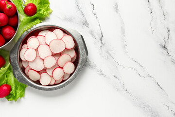 Bowls with fresh slices of radish and lettuce on marble background