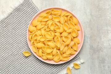 Plate with raw conchiglie pasta on grunge background