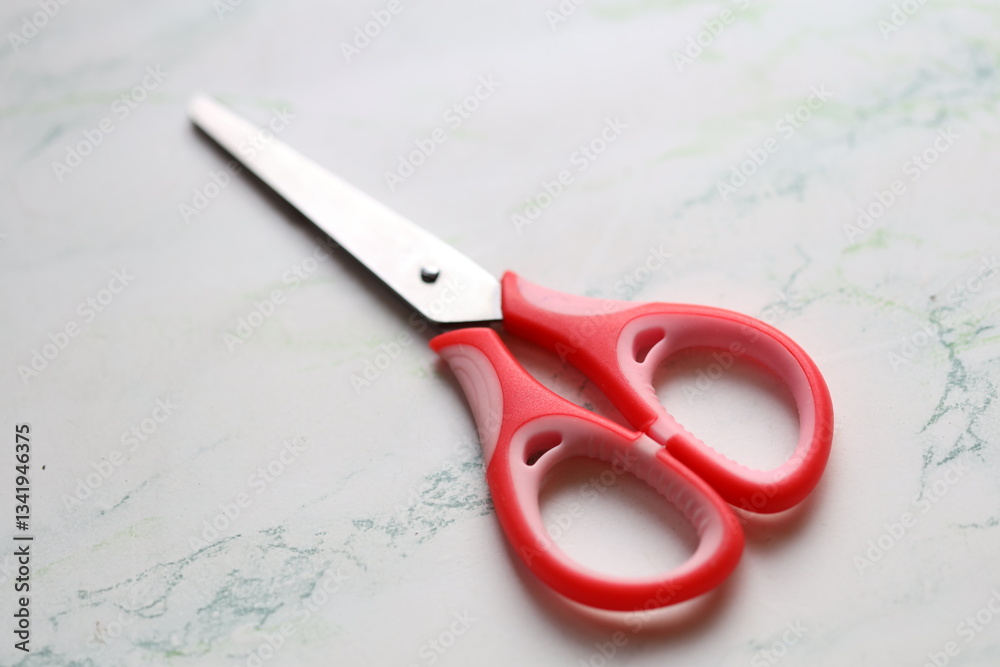 Poster A pair of red scissors resting on a table, ideal for photography, graphic design, or any other context where a sharp object is needed.
