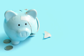 Broken patched piggy bank with money on blue background. Bankruptcy concept