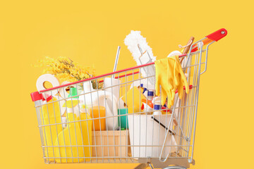 Shopping cart full of cleaning supplies with flowers on yellow background