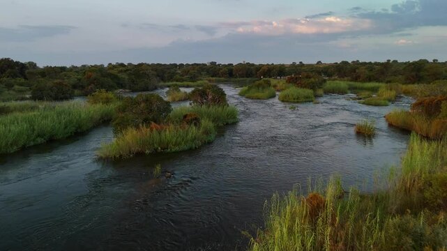 Aerial drone view of the Okavango River at sunrise on the Namibia-Angola border, Africa. The river features a shore and green vegetation.