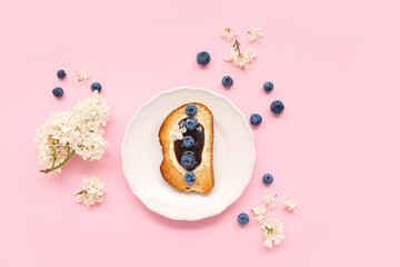 Plate with delicious jam toast, blueberries and flowers on pink background