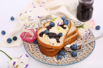 Plate with delicious jam toasts, blueberries and flowers on white background