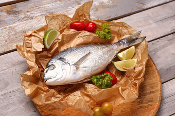 Board of raw dorado fish with lime and tomatoes on grey wooden background