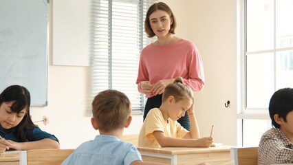 Energetic smart teacher explain classwork to caucasian boy at classroom while multicultural student...