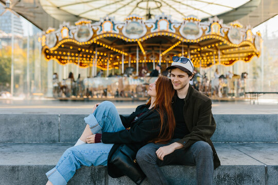 Young couple relaxing by a carousel, enjoying a sunny day in New York - Powered by Adobe