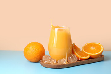 Board and glass of fresh orange juice with splashes on table against beige background