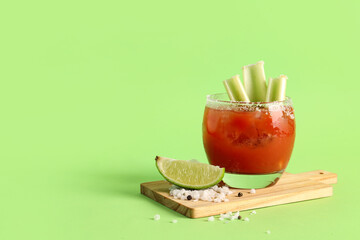 Board with glass of bloody mary and celery on green background