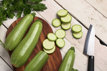 Board with many fresh green zucchini and parsley on white wooden background