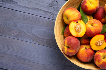 Bowl with sweet peaches and leaves on blue wooden background