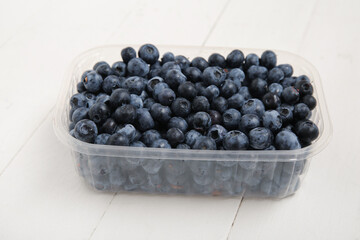 Plastic container with fresh blueberry on light wooden background, closeup