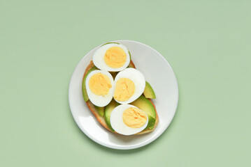 Plate of toast with boiled eggs and avocado on green background
