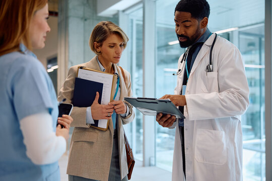 Healthcare workers and businesswoman going through paperwork during meeting in hospital.